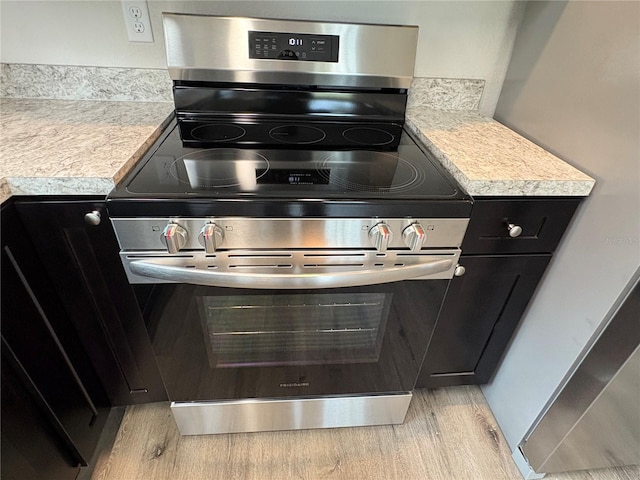 room details featuring stainless steel range with electric stovetop, light wood-style flooring, light countertops, and dark cabinetry