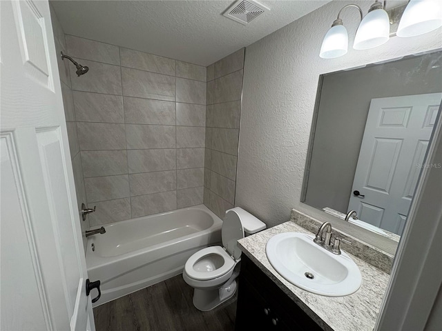 full bathroom with a textured ceiling, a textured wall, toilet, wood finished floors, and visible vents