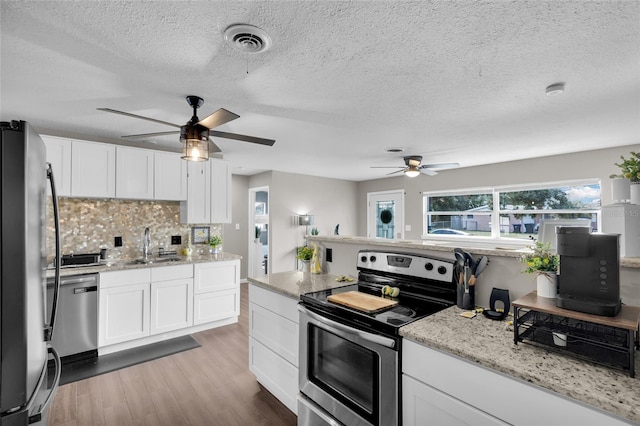 kitchen with decorative backsplash, appliances with stainless steel finishes, a textured ceiling, light hardwood / wood-style floors, and white cabinetry