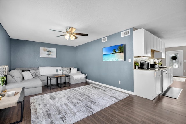 living room featuring a textured ceiling, ceiling fan, dark wood-type flooring, and sink