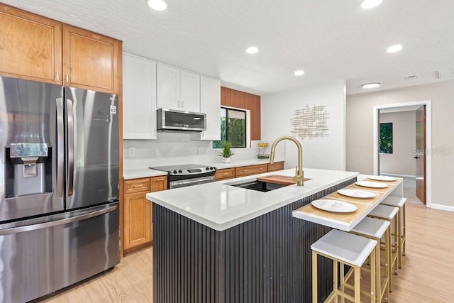 kitchen featuring a breakfast bar, a kitchen island with sink, sink, appliances with stainless steel finishes, and white cabinetry