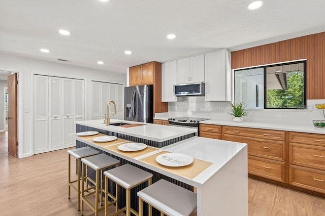 kitchen with appliances with stainless steel finishes, light hardwood / wood-style flooring, a kitchen island with sink, and a breakfast bar area