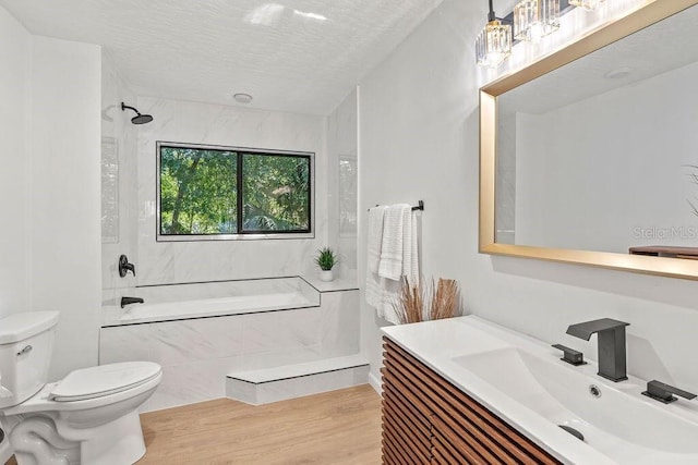 full bathroom featuring a textured ceiling, vanity, tiled shower / bath combo, wood-type flooring, and toilet