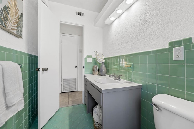 bathroom featuring tile patterned flooring, vanity, toilet, and tile walls