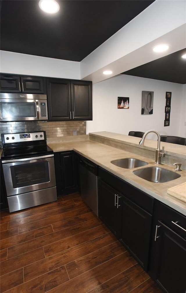 kitchen with kitchen peninsula, appliances with stainless steel finishes, tasteful backsplash, sink, and dark hardwood / wood-style floors