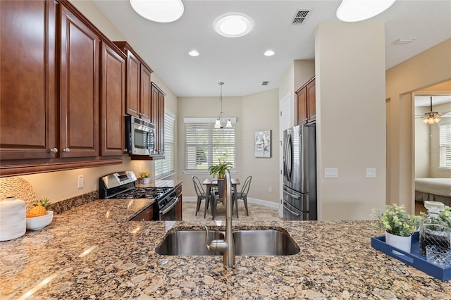 kitchen with ceiling fan with notable chandelier, sink, stainless steel appliances, and stone counters