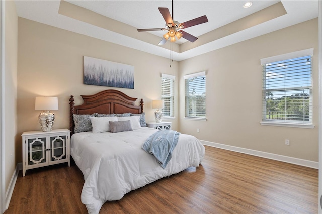 bedroom featuring a raised ceiling, ceiling fan, dark hardwood / wood-style flooring, and multiple windows