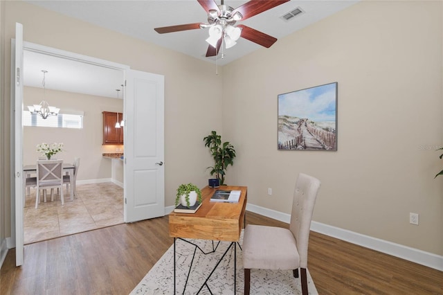 office with ceiling fan with notable chandelier and light wood-type flooring