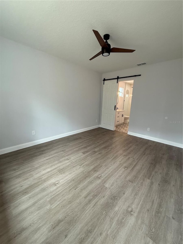 unfurnished room with hardwood / wood-style floors, a barn door, a textured ceiling, and ceiling fan