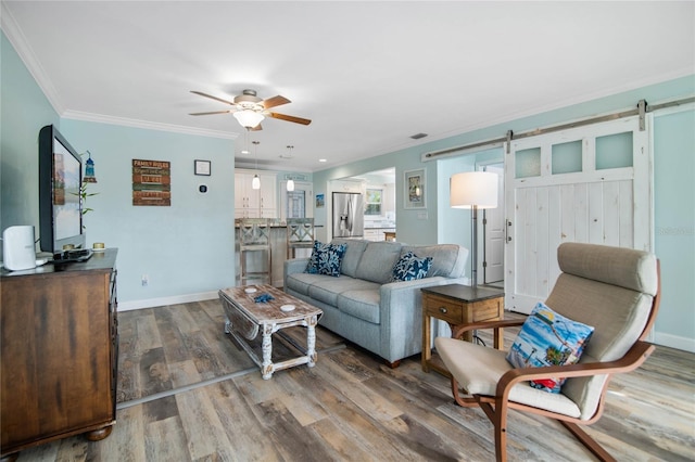 living room with a barn door, ceiling fan, wood-type flooring, and ornamental molding