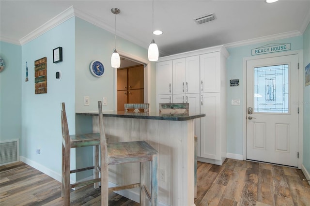 kitchen featuring pendant lighting, crown molding, dark hardwood / wood-style floors, a kitchen bar, and white cabinetry