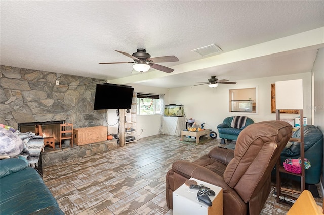 living room with hardwood / wood-style flooring, ceiling fan, a stone fireplace, and a textured ceiling