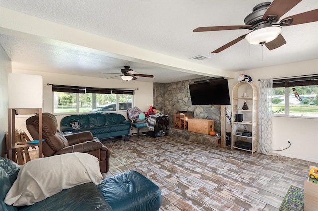 living room with a textured ceiling, ceiling fan, and a fireplace