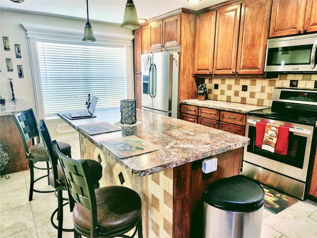 kitchen with hanging light fixtures, light tile patterned floors, appliances with stainless steel finishes, light stone counters, and a breakfast bar area