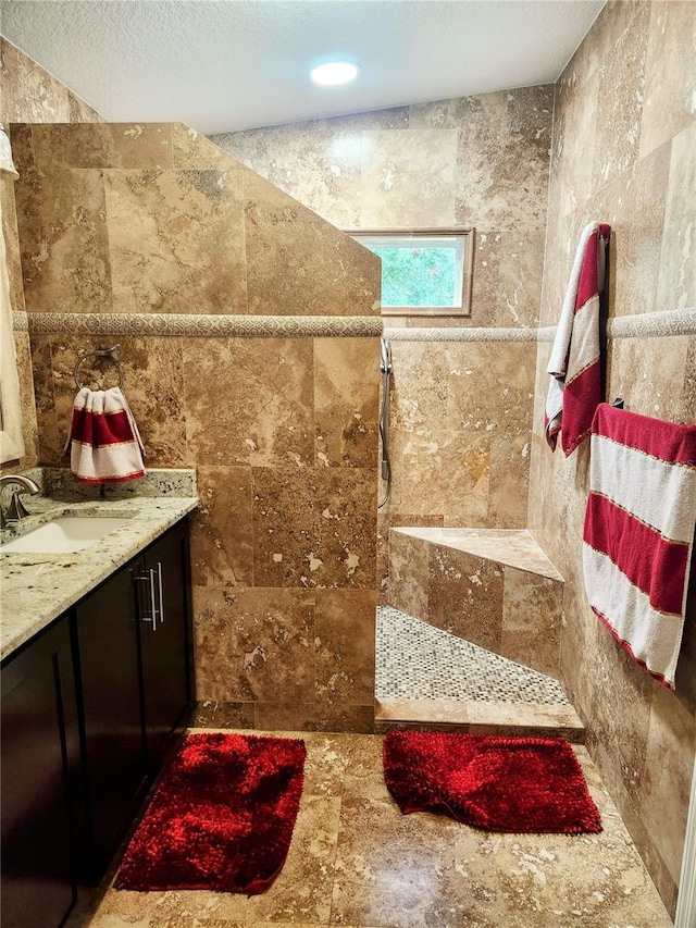 bathroom with tiled shower, vanity, and tile walls