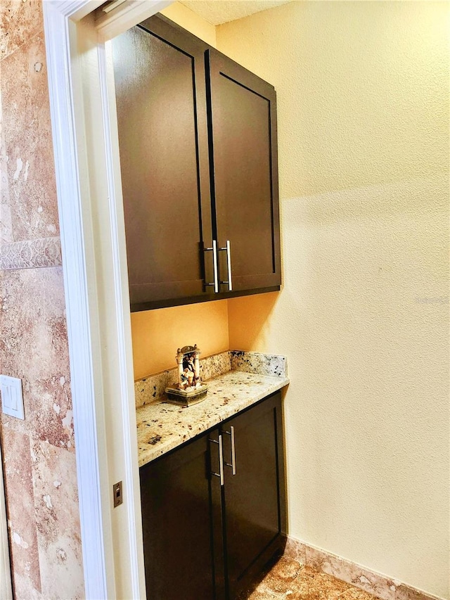 bar featuring dark brown cabinetry and light stone counters