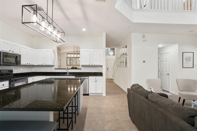 kitchen with hanging light fixtures, dark stone countertops, a kitchen bar, white cabinets, and appliances with stainless steel finishes