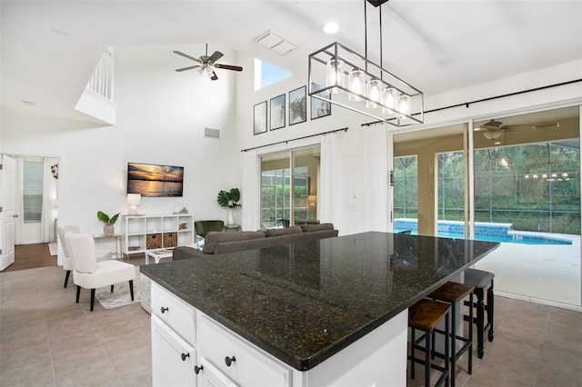 kitchen with a kitchen island, high vaulted ceiling, dark stone countertops, decorative light fixtures, and white cabinets