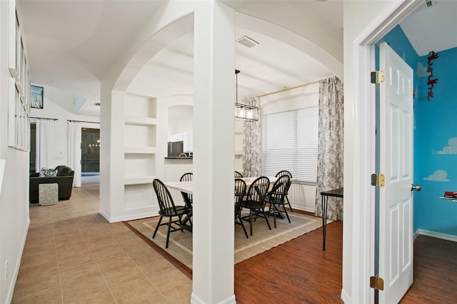 dining area with vaulted ceiling, light hardwood / wood-style floors, built in features, and an inviting chandelier