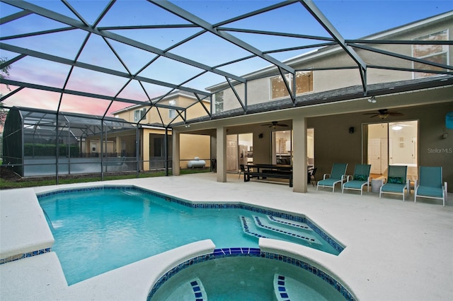 pool at dusk featuring an in ground hot tub, a patio, ceiling fan, and a lanai