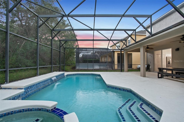 pool at dusk with glass enclosure, ceiling fan, pool water feature, and a patio