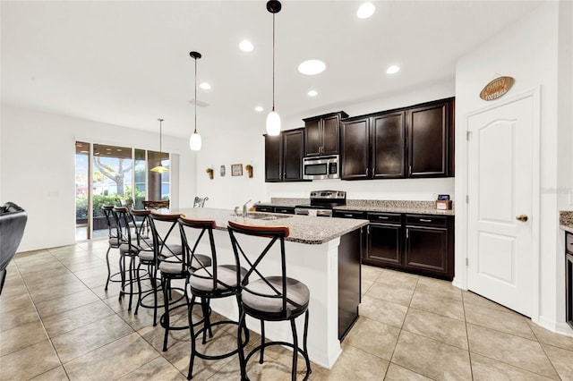 kitchen with a breakfast bar, appliances with stainless steel finishes, pendant lighting, and an island with sink