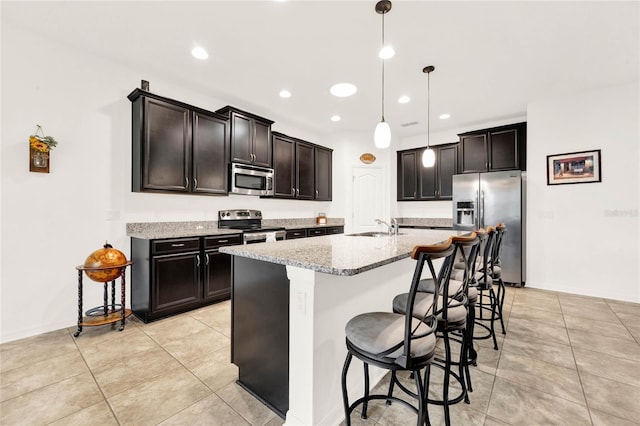 kitchen with light stone countertops, sink, an island with sink, pendant lighting, and appliances with stainless steel finishes