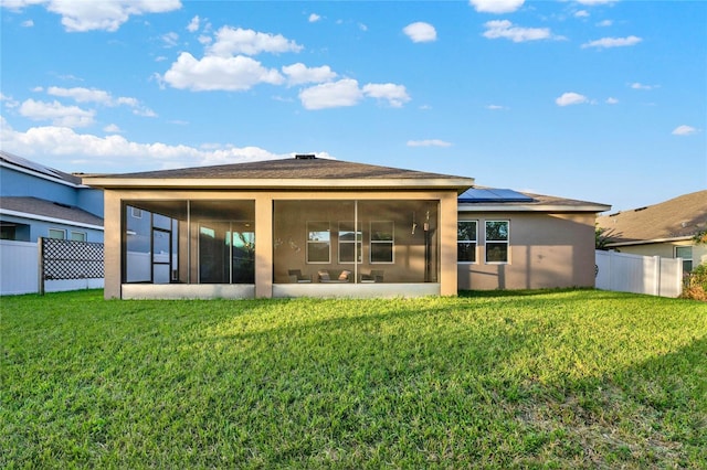 back of house featuring a lawn, a sunroom, and solar panels