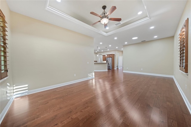 unfurnished living room featuring a raised ceiling, ceiling fan, dark wood-type flooring, and ornamental molding