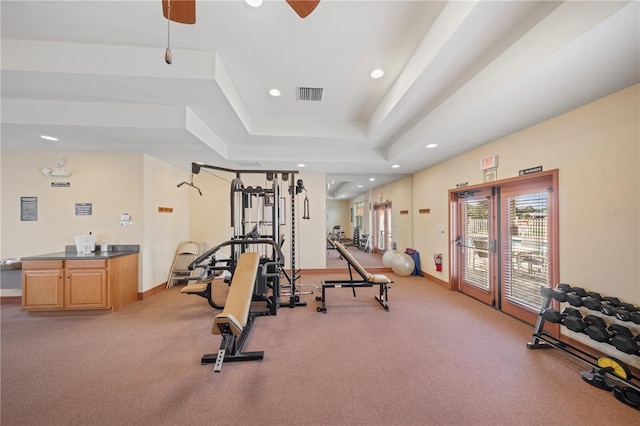 workout room with a tray ceiling and ceiling fan