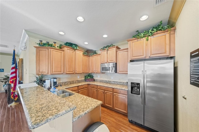 kitchen featuring a kitchen breakfast bar, light brown cabinetry, appliances with stainless steel finishes, light hardwood / wood-style floors, and kitchen peninsula