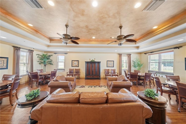 living room featuring ceiling fan, wood-type flooring, and a tray ceiling