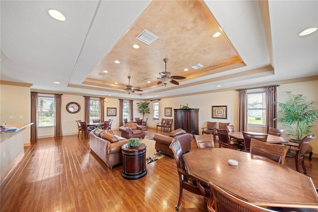 living room featuring ceiling fan, a raised ceiling, and light wood-type flooring