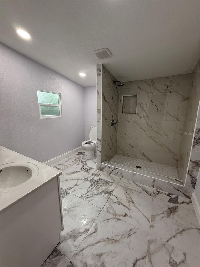 bathroom featuring a tile shower, vanity, a textured ceiling, and toilet