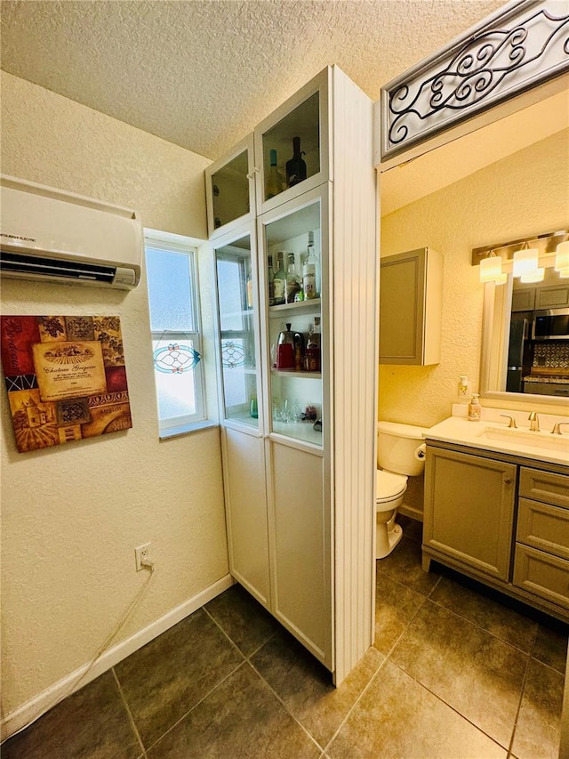 interior space featuring tile patterned flooring, a wall unit AC, a textured ceiling, toilet, and vanity