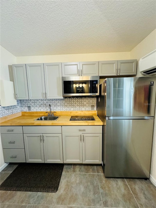 kitchen featuring butcher block counters, sink, stainless steel appliances, tasteful backsplash, and a wall mounted AC