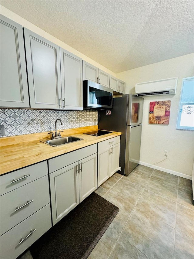 kitchen featuring appliances with stainless steel finishes, tasteful backsplash, a wall mounted AC, sink, and butcher block counters