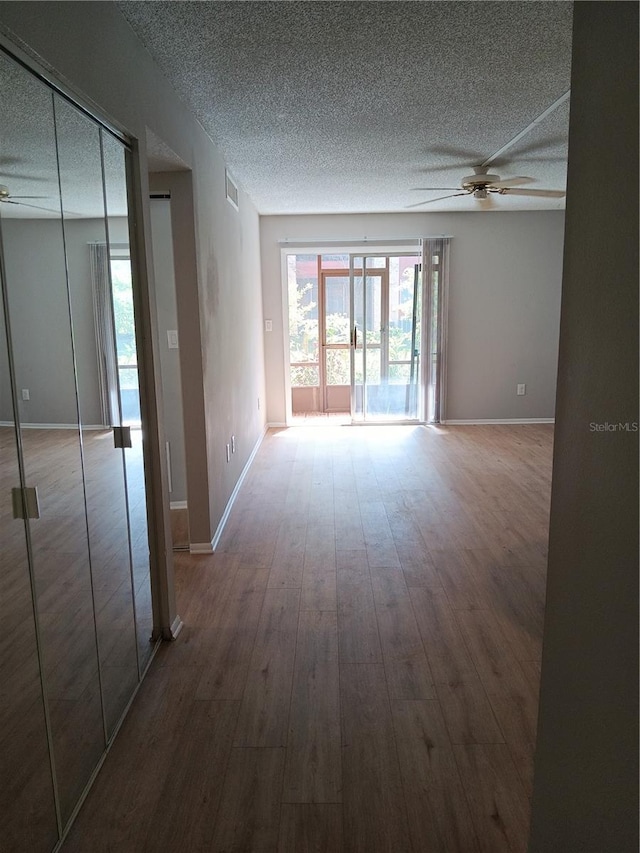 empty room featuring visible vents, a textured ceiling, wood finished floors, and a ceiling fan