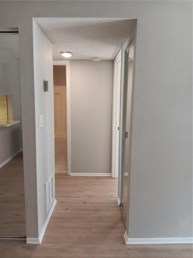 corridor featuring light wood-type flooring, visible vents, and baseboards