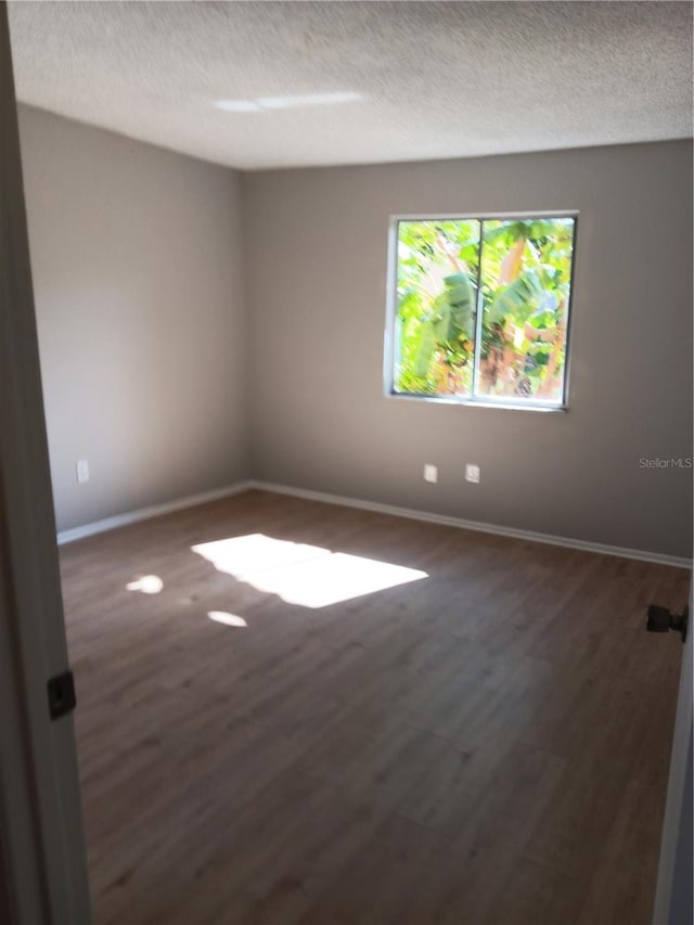 spare room featuring a textured ceiling, dark wood-style floors, and baseboards