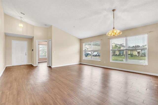 unfurnished room with hardwood / wood-style flooring, lofted ceiling, an inviting chandelier, and a textured ceiling