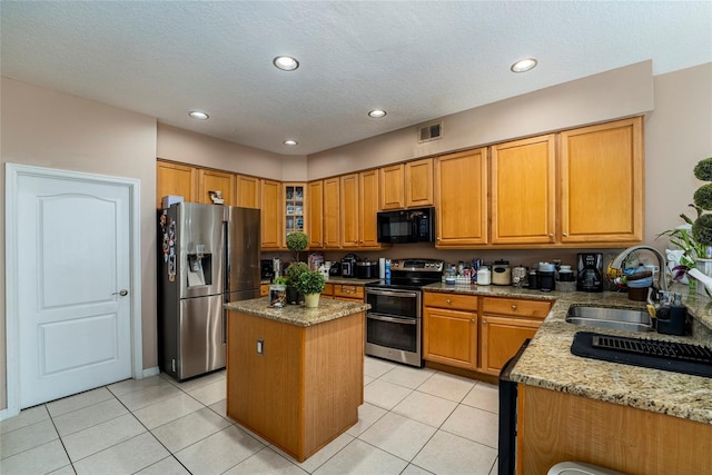 kitchen with a center island, sink, light stone countertops, light tile patterned floors, and stainless steel appliances