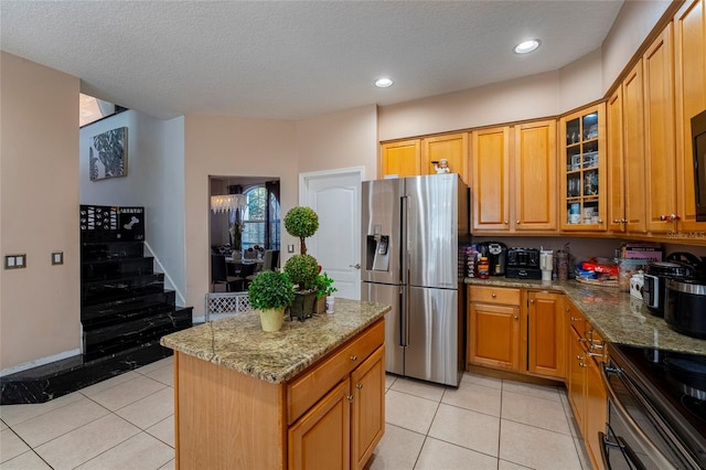 kitchen with stainless steel fridge, a kitchen island, light stone countertops, and a textured ceiling