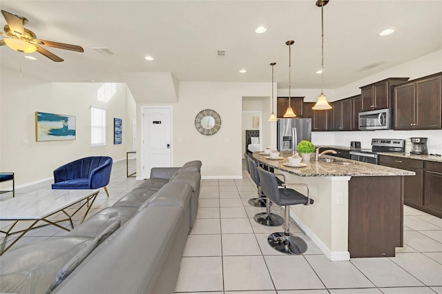 2468 Dubai St, Kissimmee, FL 34747 - kitchen with appliances with stainless steel finishes, open floor plan, dark brown cabinetry, light tile patterned floors, and light stone counters