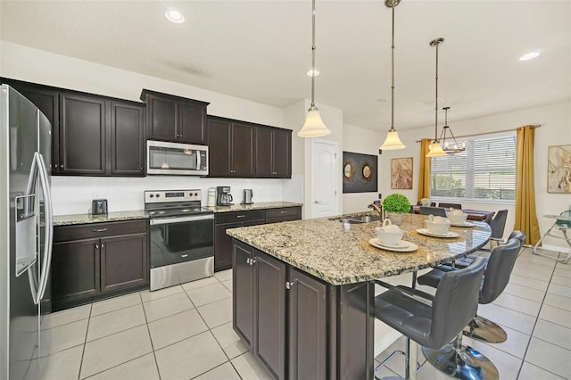 kitchen with dark brown cabinetry, a kitchen island with sink, decorative light fixtures, and appliances with stainless steel finishes