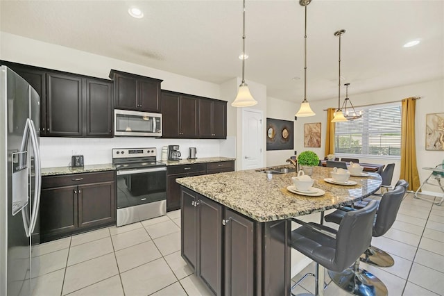 2468 Dubai St, Kissimmee, FL 34747 - kitchen with stainless steel appliances, a kitchen bar, light tile patterned flooring, a center island with sink, and light stone countertops