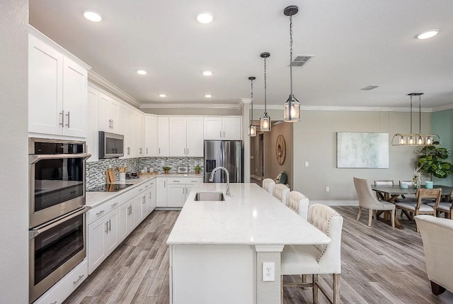 kitchen featuring appliances with stainless steel finishes, a breakfast bar, a center island with sink, light hardwood / wood-style flooring, and white cabinetry