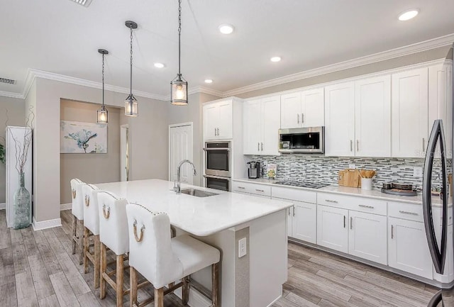 kitchen with light wood-type flooring, stainless steel appliances, pendant lighting, white cabinets, and an island with sink