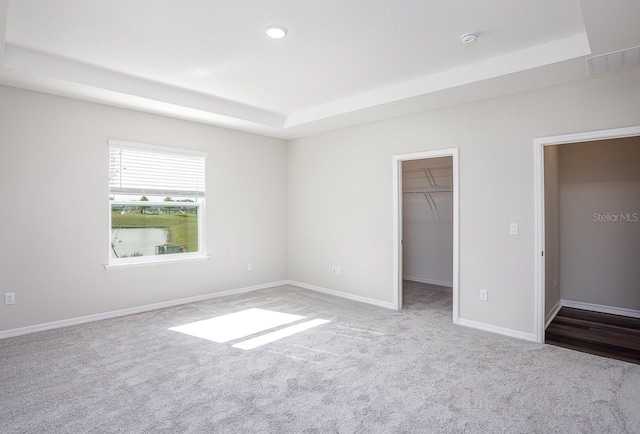 unfurnished bedroom featuring a tray ceiling, a walk in closet, light carpet, and a closet