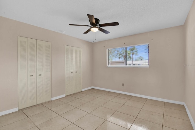 unfurnished bedroom featuring a textured ceiling, ceiling fan, light tile patterned floors, and two closets